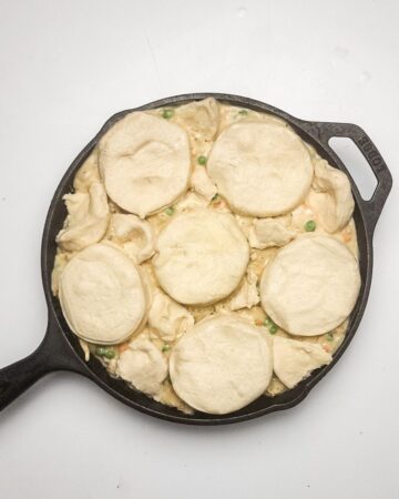 A cast iron pan with creamy chicken and ingredients to make chicken pot pie with biscuits. 