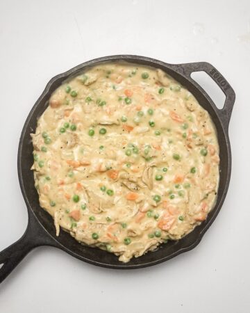 A large cast iron pan with the ingredients for a chicken pot pie.