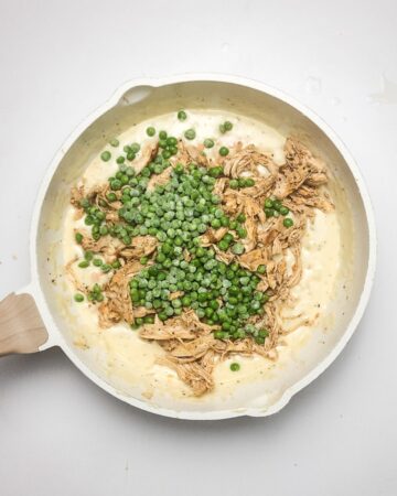 A saute pan with chicken and peas in a creamy sauce for a chicken pot pie.
