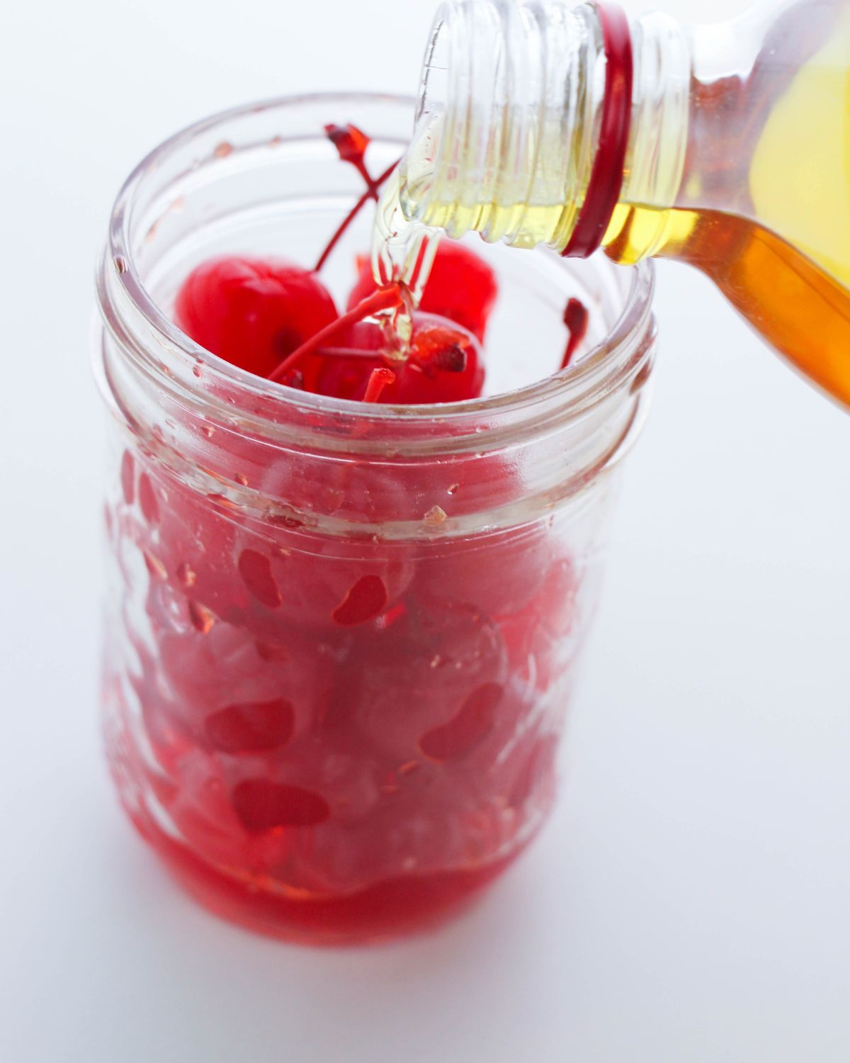 A mason jar with cherries with fireball being poured over the cherries.
