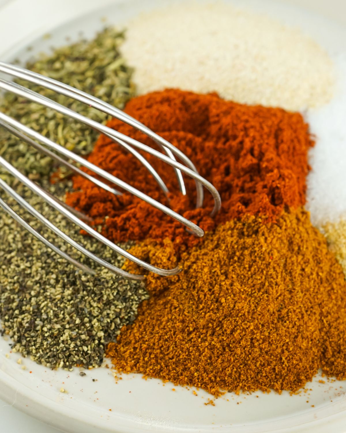 A whisk in a bowl of various seasoning to make a homemade seasoning blend. 