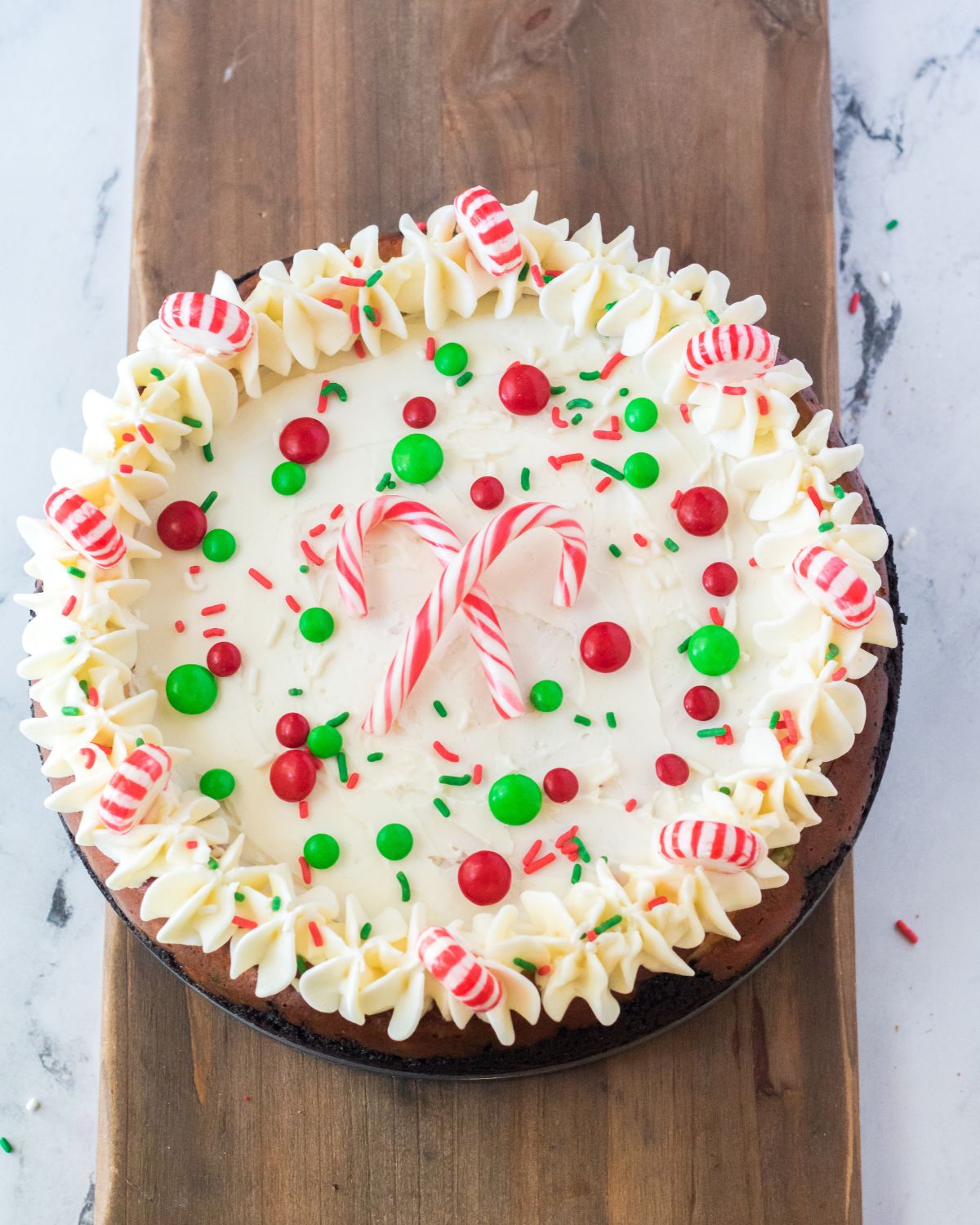 A decorated cheesecake with peppermint candies, candy canes, and candy coated chocolates.