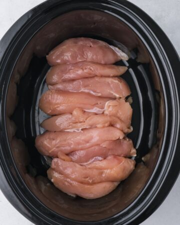 A slow cooker with chicken in the pot to make broccoli rice chicken. 