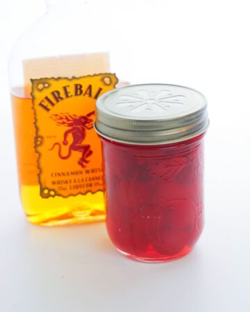 Mason jar with whiskey infused maraschino cherries with a fireball whiskey in the back.