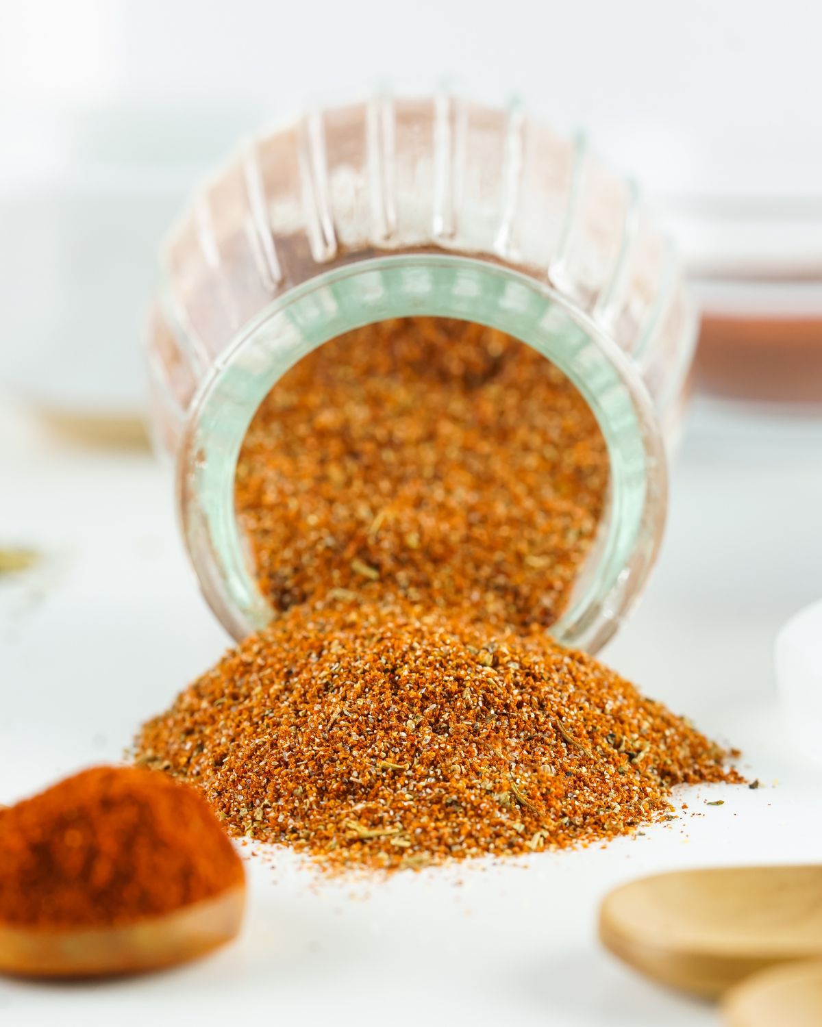 A glass jar with a spill of blackened seasoning put and about.
