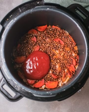 An instant pot with lentils, carrots, and fire roasted tomatoes to make lentil stew. 