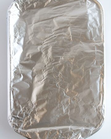 A casserole dish covered with aluminum foil to make oven baked fried rice.