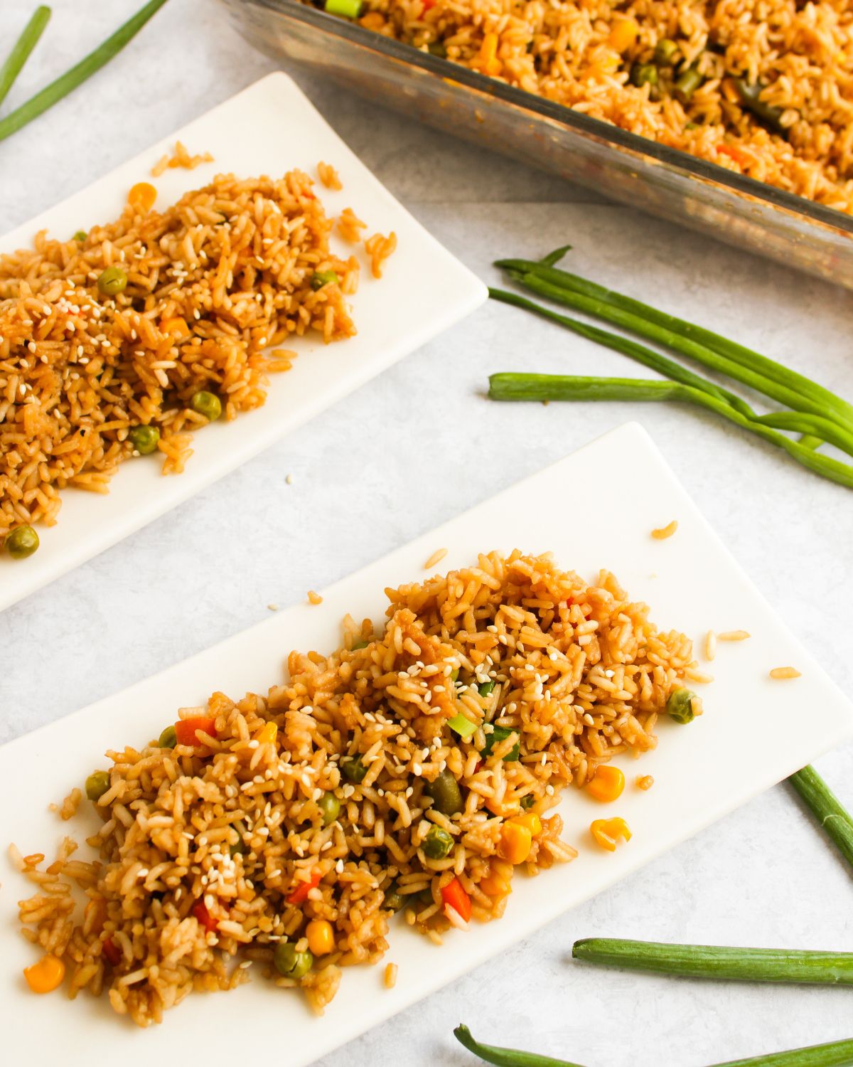 Oven baked fried rice on white plates with green onions on the side.