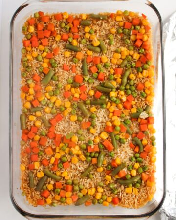 A glass casserole dish with rice and vegetables to make baked fried rice.
