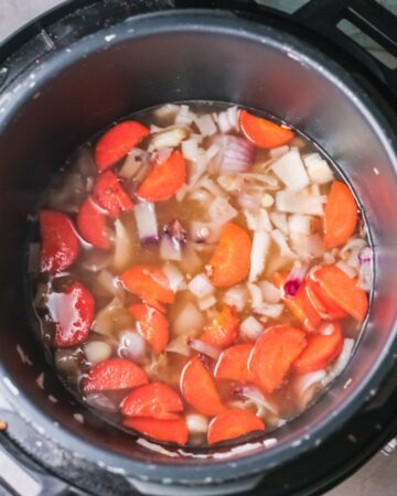 An instant pot vessel with carrots, onions, lentils, and vegetable broth.