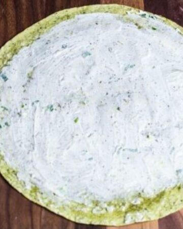 A spinach tortilla with a cream cheese spread on the tortilla.