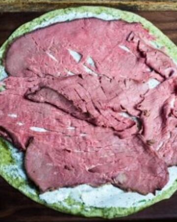 A tortilla with cream cheese and roast beef to make a tortilla wrap.