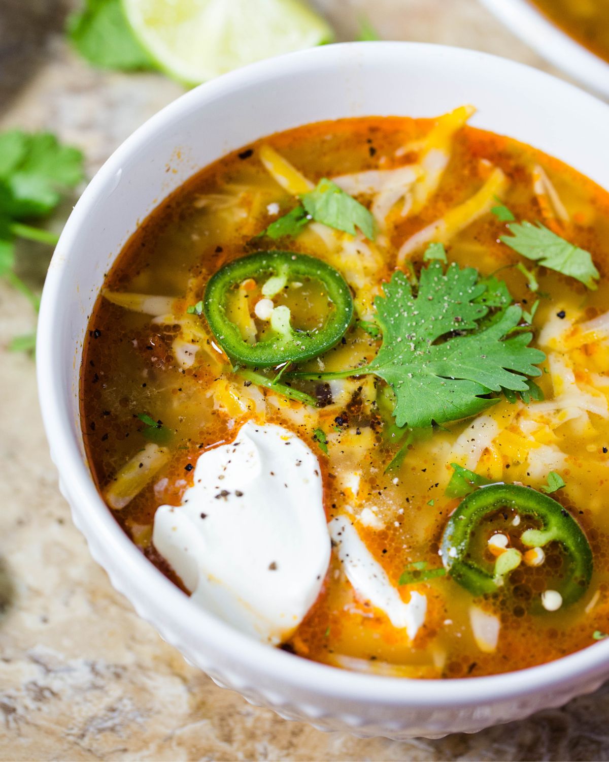 A bowl of chicken enchilada soup in a bowl topped with jalapenos, cheddar cheese, and soup cream.