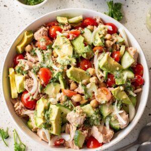 A white bowl with chickpea tuna avocado salad with a honey dijon dressing.