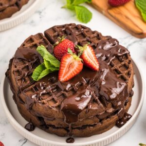Chocolate waffles topped with chocolate syrup, sliced strawberries, and mint leaves.