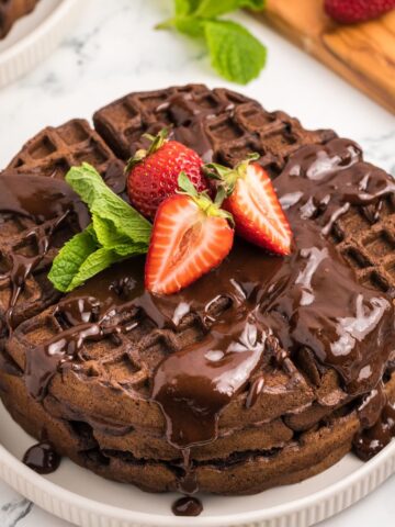 Chocolate waffles topped with chocolate syrup, sliced strawberries, and mint leaves.