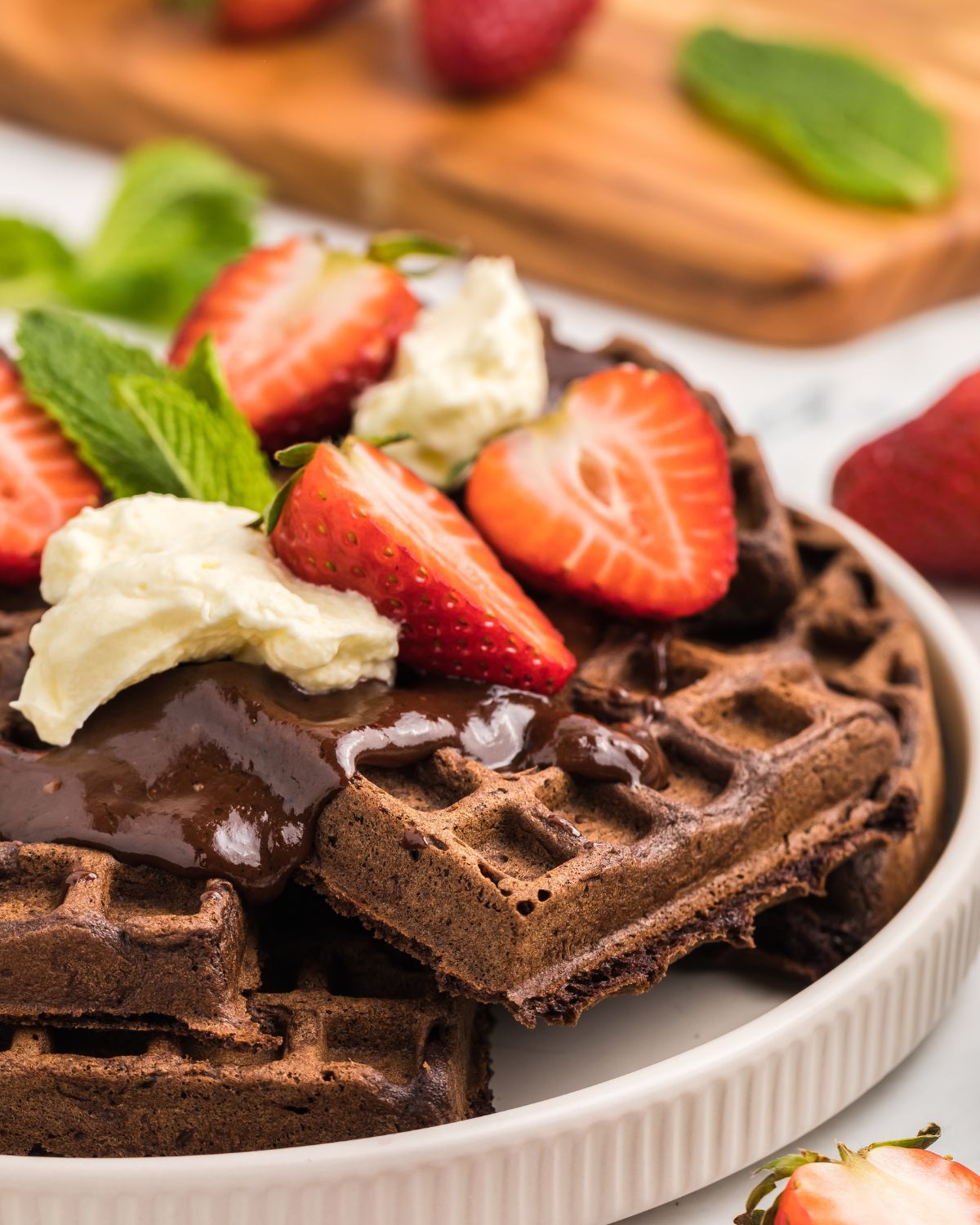 A stack of chocolate waffles topped with chocolate sauce, sliced strawberries, and vanilla ice cream.