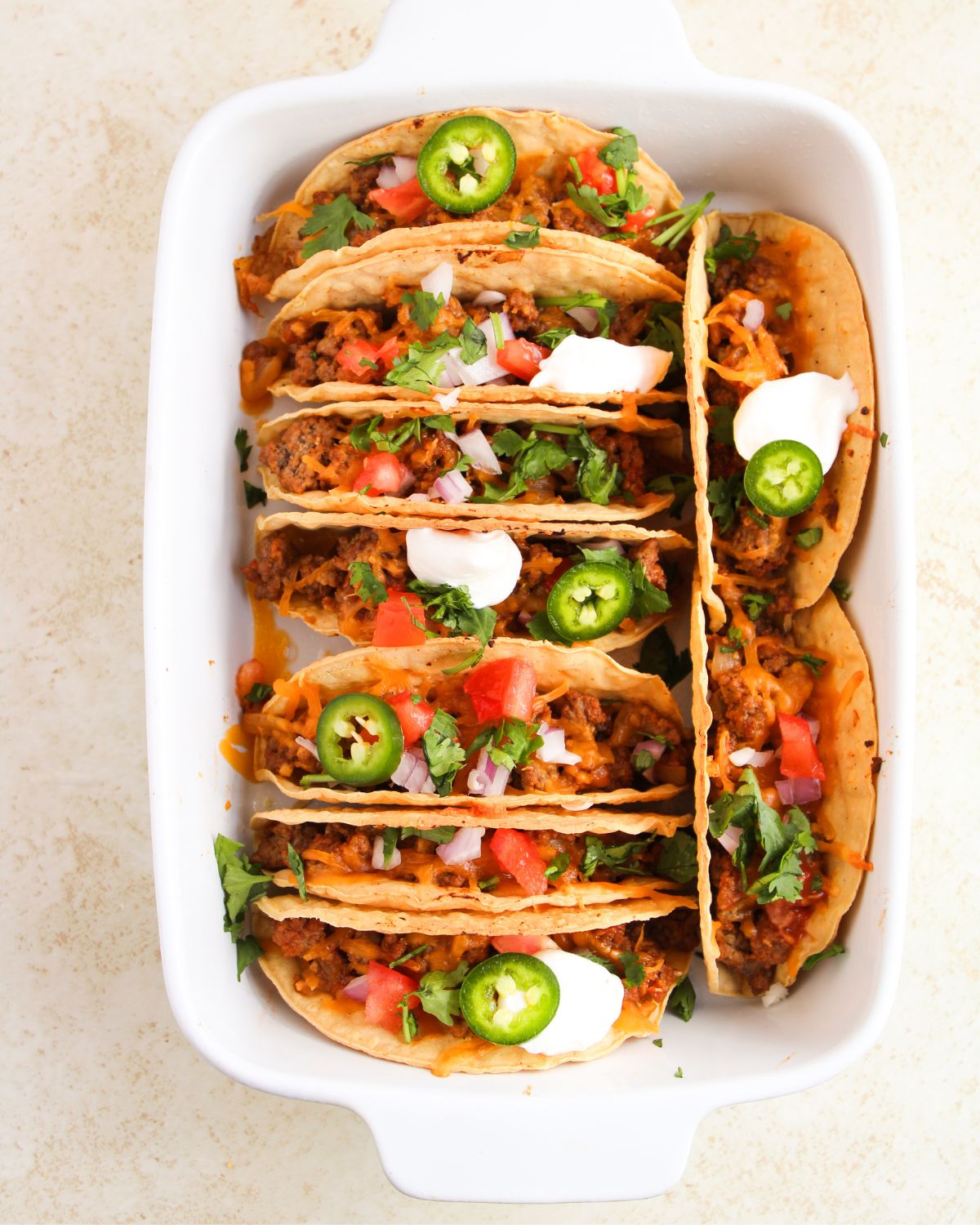 A casserole baking pan with hard tacos with seasoned ground beef and cheddar cheese.