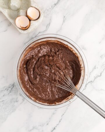A class bowl with wet and dry ingredients combined to make chocolate waffles. 