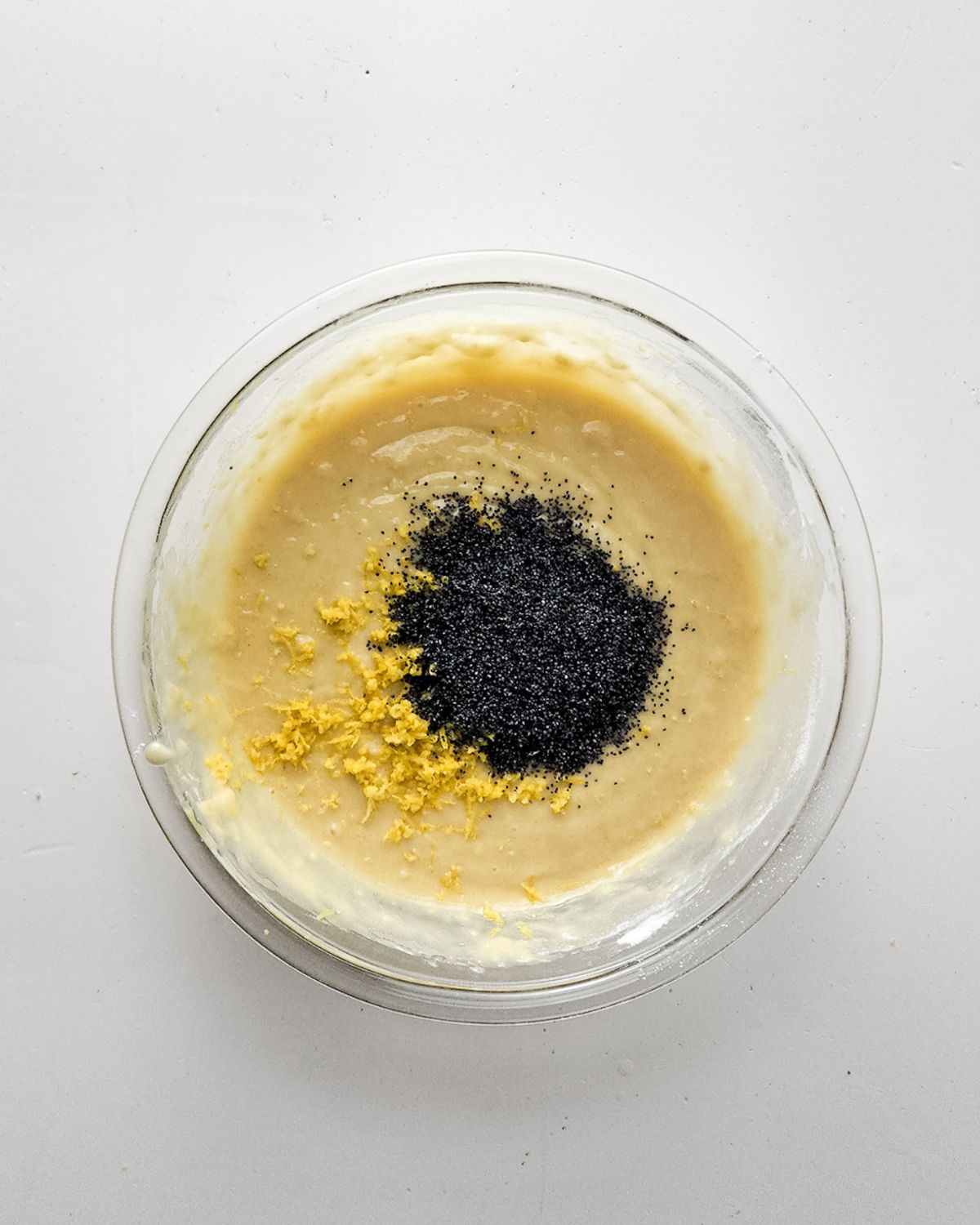 A mixing bowl with lemon poppyseed batter with lemon zest and poppyseed.
