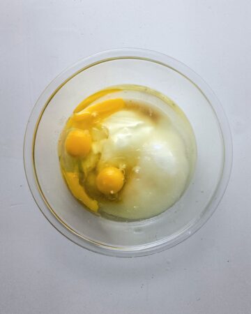 A mixing bowl with eggs, yogurt, and sugar to make a lemon poppy seed loaf.