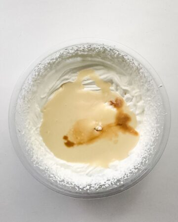 A glass mixing bowl with whipped cream and ingrdients to make homemade mint oreo ice cream.