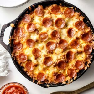 A cast iron skillet with pasta and a pizza topping with pepperoni.