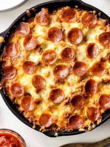 A cast iron skillet with pasta and a pizza topping with pepperoni.