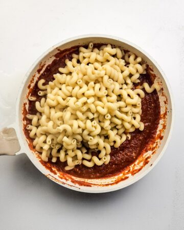 A saute pan with marinara sauce and cavatappi pasta to make a pizza pasta bake.