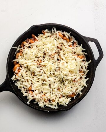 A cast iron pn with pasta and marinara with mozzarella to make a pasta bake.