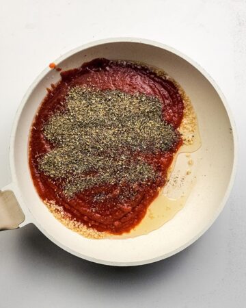 A saute pan with marinara sauce and seasoning to make the sauce for a pizza pasta bake.