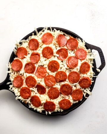 A cast iron pan with pasta and red sauce topped with cheese and pepperoni for a pizza pasta dinner. 