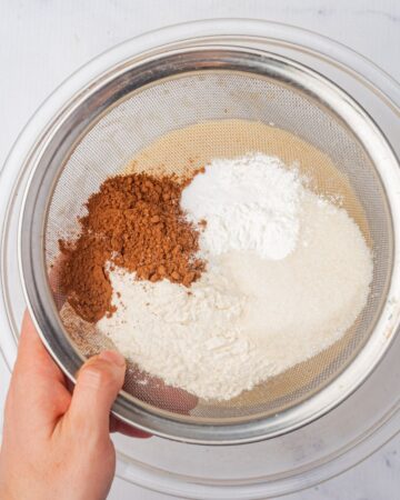 Dry ingredients being sifted into a glass mixing bowl to make homemade baileys cupcakes.