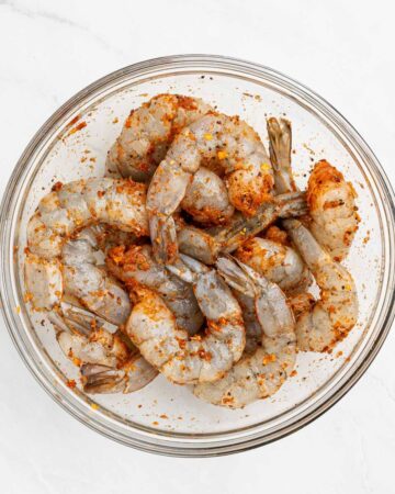 A large mixing bowl with shrimp sprinkled with Cajun seasoning.