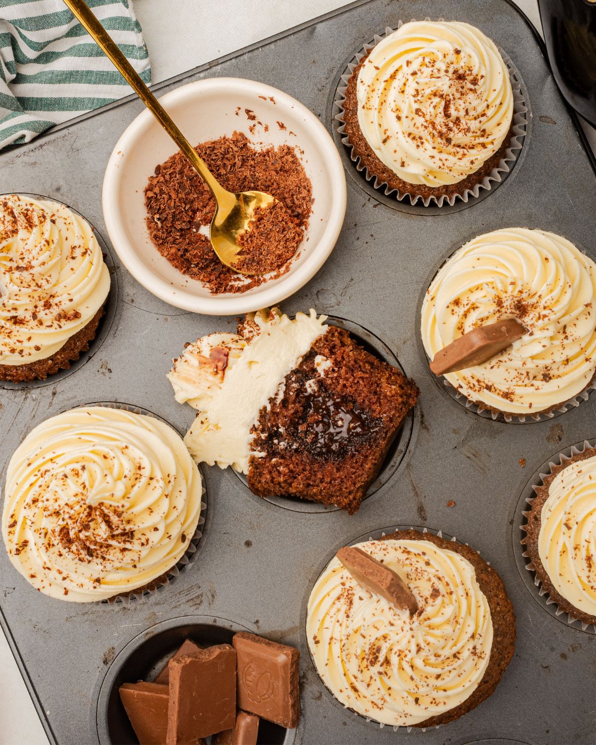 Muffin tin with decorated Irish Cream cupcakes and some cut in half to show the chocolate center.