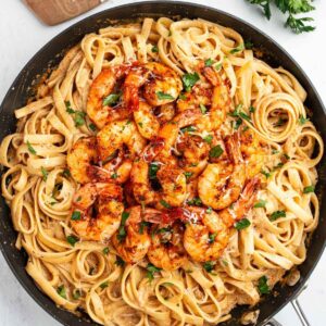 A large pan with fettuccini topped with Cajun shrimp.