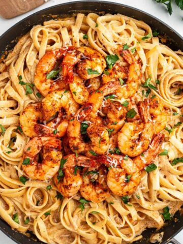 A large pan with fettuccini topped with Cajun shrimp.