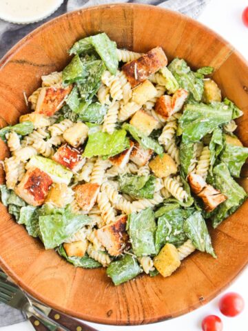 A wooden salad bowl with creamy chicken caesar salad pasta recipe.