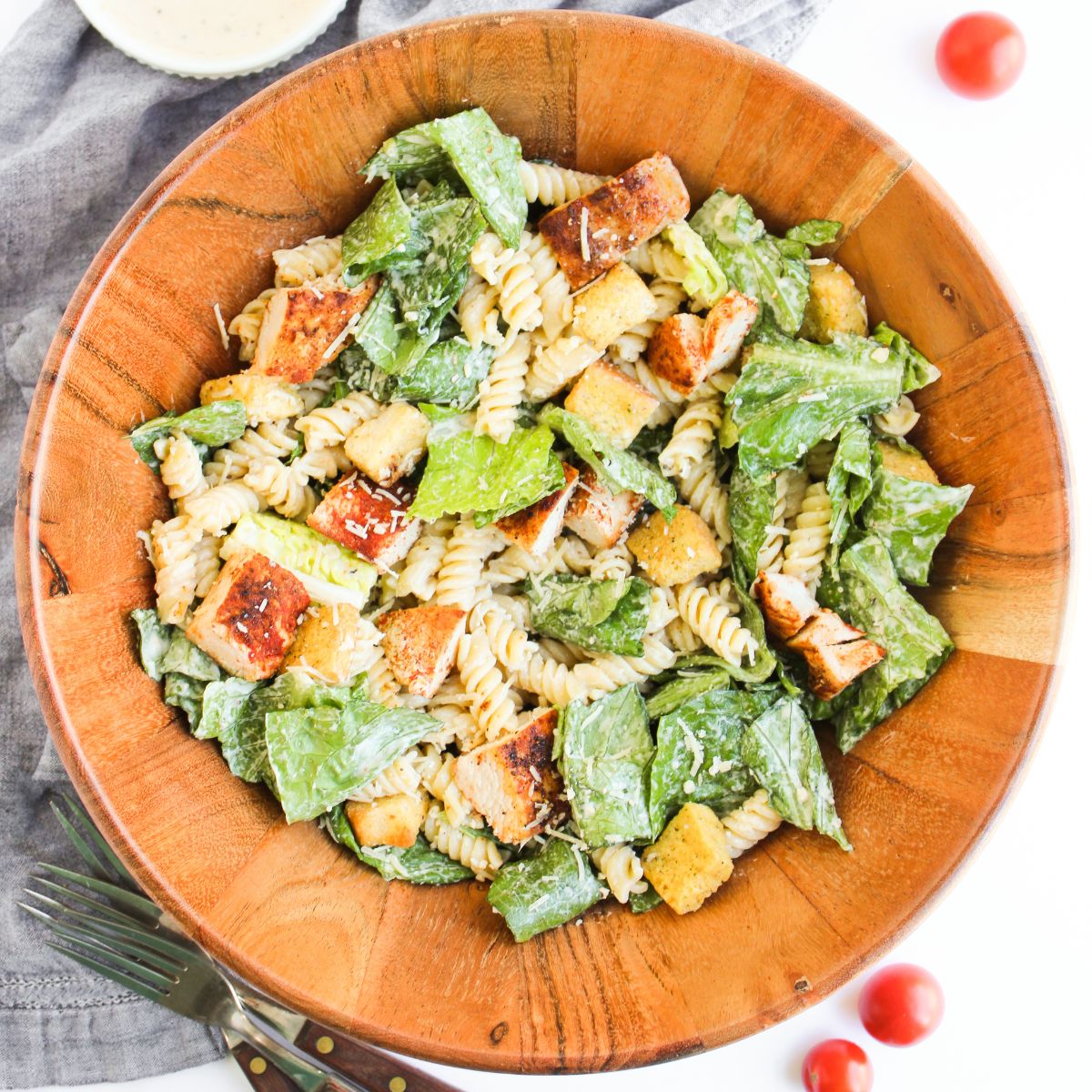 A wooden salad bowl with creamy chicken caesar salad pasta recipe.