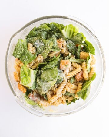 The ingredients to make chicken caesar pasta salad in a bowl after being mixed together.