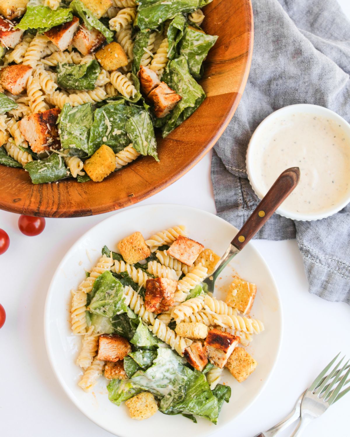 A plate of chicken caesar pasta salad and the wooden bowl of the rest of the salad behind the plate.