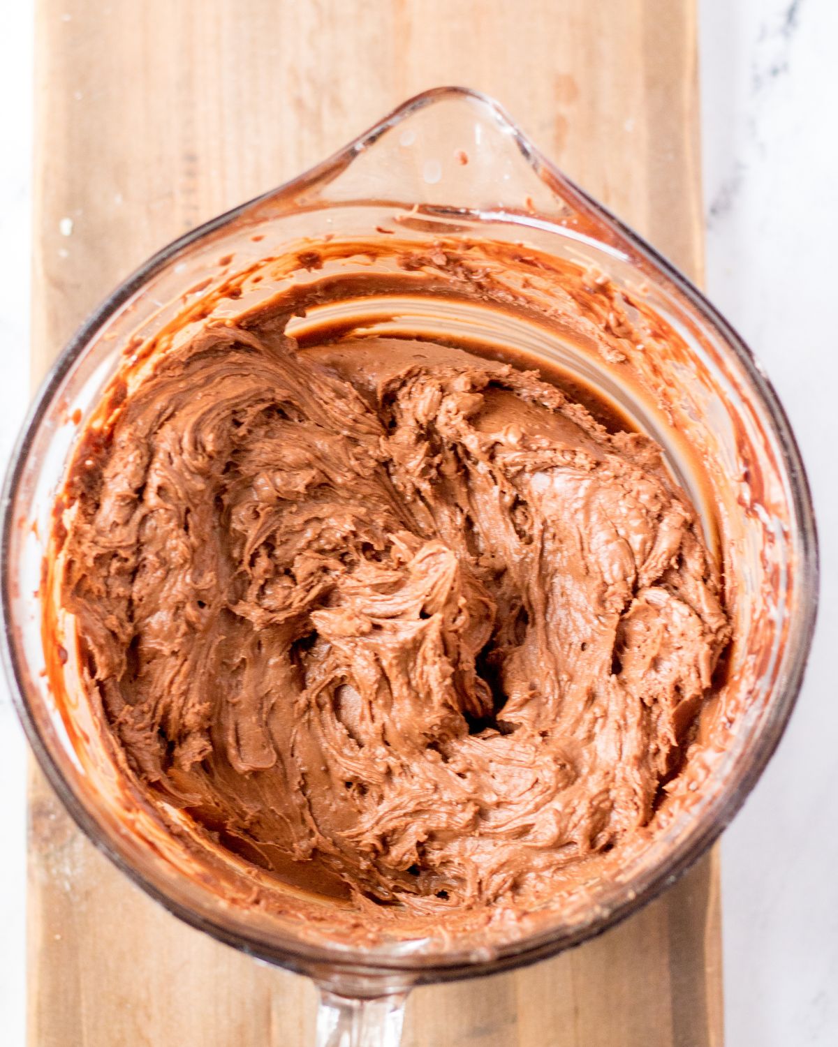 A glass measuring cup with chocolate frosting to go on a chocolate cake. 
