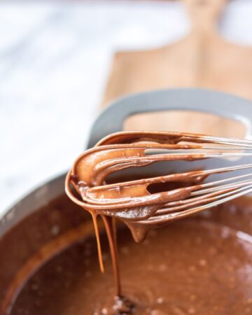 A whisk with the begining of a chocolate frosting for a chocolate cake.