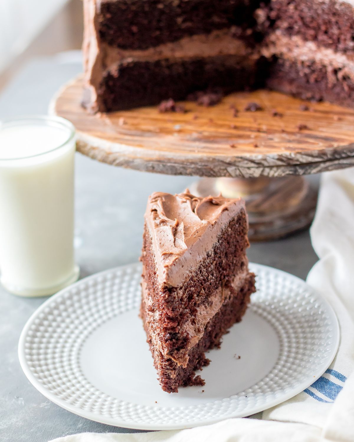 Chocolate cake slice with the cake behind on a cake platter.