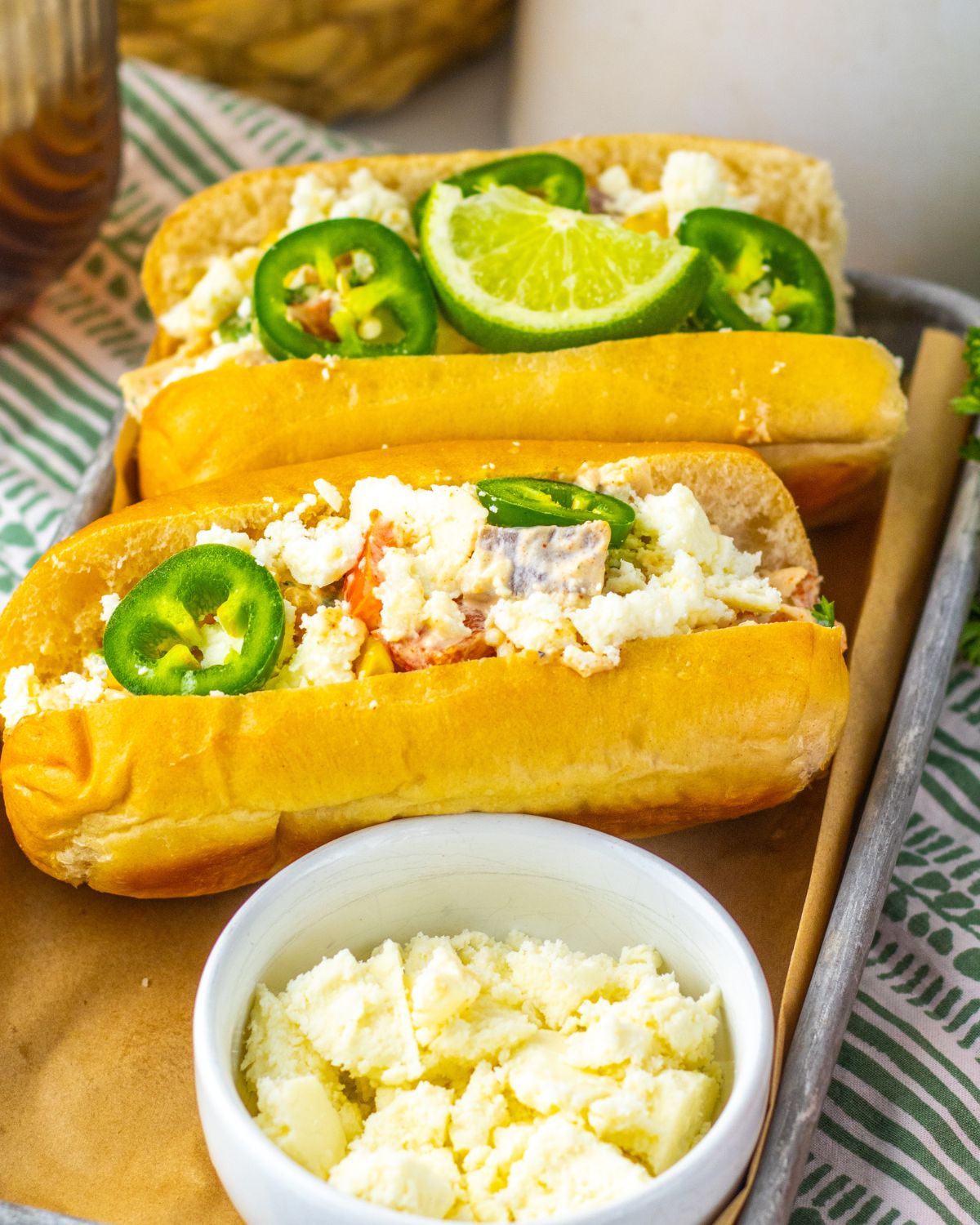 Mexican street corn chicken salad in a sliced long roll with sliced jalapeno and queso fresco.