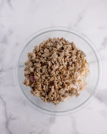 A glass bowl with browned hamburger meat and ingredients to make a creamy filling for hash brown and hamburger casserole. 