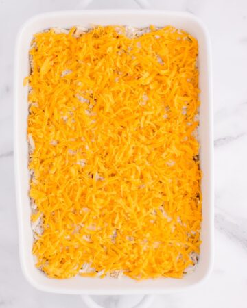 A casserole dish with ground beef, hash browns, topped with cheddar cheese to bake in the oven. 