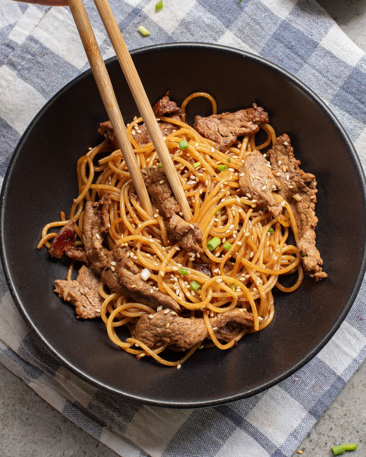 A large black bowl with cooked hibachi noodles and steak with sesame seeds and chopped green onions.