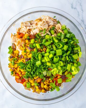 A glass bowl with chicken, corn, herbs, and green onion to make Mexican street corn chicken salad.