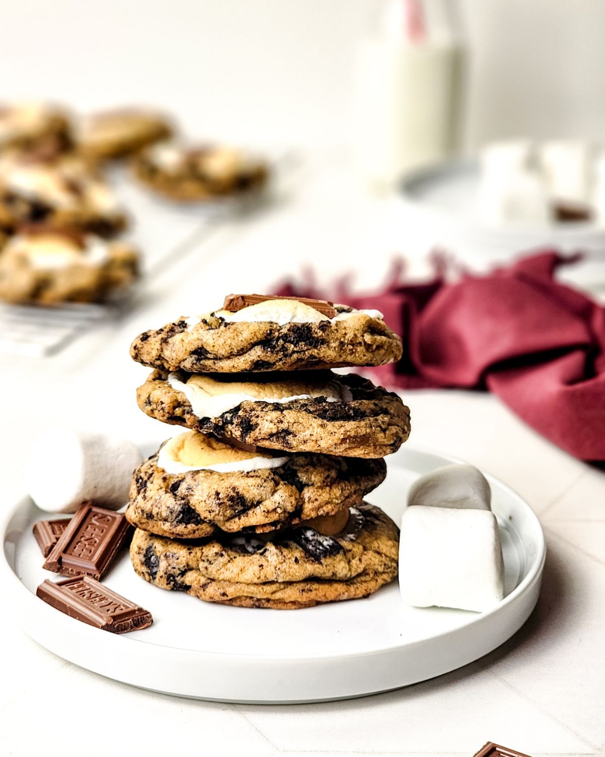 A stack of s'mores cookies with hershey bars on the side and marshmallows on the opposite side. 